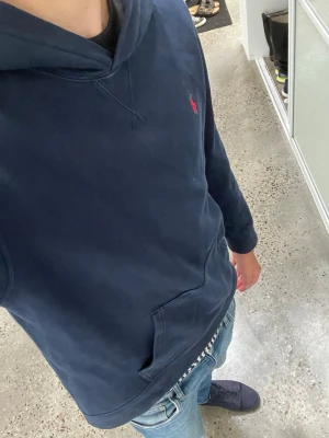 Ralph lauren  - Snygg mörkblå hoodie med huva och känguruficka framtill. På bröstet finns en liten röd broderad logga som ger en clean och stilren look. Perfekt till jeans och sneakers för en avslappnad stil.