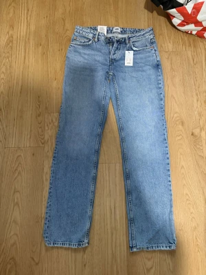 Ljusblå raka jeans med låg midja - Säljer ett par ljusblå jeans med rak passform och låg midja. Klassisk femficksmodell och gylf med dragkedja och knapp. Jeansen har en tidlös look och är tillverkade i denim, perfekt för en avslappnad stil.