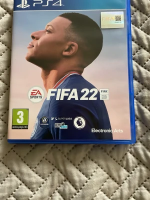 FIFA 22 till PS4 och ps5 - FIFA 22 till PlayStation 4, ett fotbollsspel från EA Sports. Blå plastfodral med omslag där en fotbollsspelare syns. Inuti finns spelmanual och Blu-ray-skiva med svart och blå design. Perfekt för dig som gillar sportspel och att bygga ditt eget lag. Det bara att skriva vid minsta aningar och pris kan diskuteras