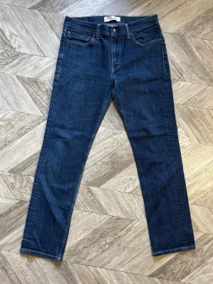 Levi's 511 - Klassiska mörkblå jeans från Levi's med rak passform och fem fickor. Jeansen har en tidlös look med diskreta sömmar och Levi's ikoniska läderpatch bak i midjan. Tillverkade i slitstark denim med en snygg tvätt. Längd 99cm Bredd 39cm
