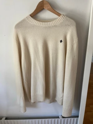 Vit stickad tröja från Morris - Klassisk vit stickad tröja från Morris med rund halsringning och diskret logga broderad på bröstet. Tröjan har ribbade muddar vid ärmslut och nederkant. Perfekt för lager på lager och enkel att matcha med olika stilar.