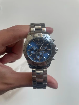 Silverfärgad klocka från BOSS - Helt ny klocka från Hugo boss. Gjort av steel och längden är ungefär 22 cm (17 cm om man inte räknar med själva klockan). Klockan är perfekt till både vardag och fest. Jag kan själv ändra storlek på klockan om det förfrågas. 