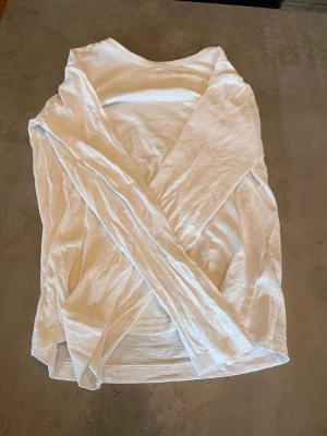 Vit långärmad basic tröja - En enkel och stilren vit långärmad tröja i mjukt och tunt material. Perfekt att ha som basplagg och funkar till det mesta. Tröjan har rund halsringning och rak passform.