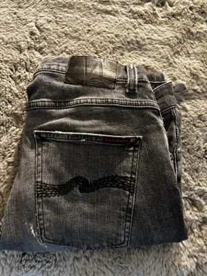 Mörkgrå Nudie Jeans Slim Fit - Säljer ett par mörkgrå slim fit jeans från Nudie Jeans. Klassisk femficksmodell med den ikoniska vågade sömmen på bakfickan. Jeansen har normal midja och är tillverkade i mjuk denim, perfekta för en avslappnad och stilren look.