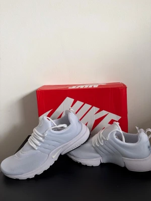 Vita Nike sneakers mesh och gummi - Snygga vita Nike sneakers med mesh-överdel och detaljer i gummi. Skorna har en sportig look med vita snören och diskret Nike-logga på sidan och tån. Perfekta för dig som gillar stilrena och bekväma sneakers.