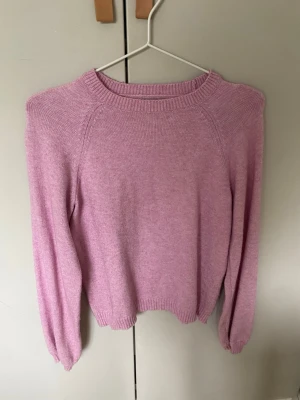 Rosa stickad tröja - Mysig rosa stickad tröja med rund halsringning och långa ärmar. Tröjan har ribbade muddar vid ärmslut och nederkant, vilket ger en skön passform. Perfekt för dig som gillar en enkel men snygg stil.