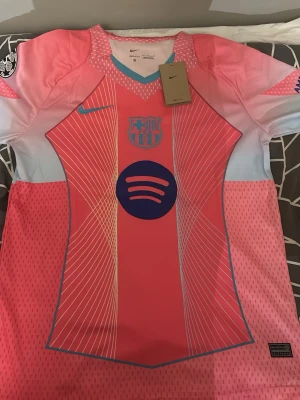Fotbolls tröja - Snygg rosa Barcelona matchtröja från Nike med blå detaljer och vitt grafiskt mönster. Tröjan har klubbmärke och sponsorlogga framtill samt patch på ärmen. Tillverkad i lätt och ventilerande material, perfekt för fotboll eller träning.