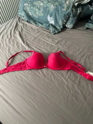 Rosa push-up bh med rosett - Snygg rosa push-up bh med vadderade kupor och liten rosett mellan kuporna. Justerbara axelband och hakknäppning bak. Perfekt för dig som vill ha extra lyft och en feminin look.