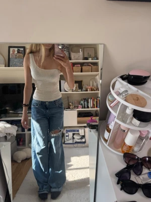 Vit oneshoulder topp med strukturmönster - Säljer en vit oneshoulder topp med snygg struktur och diskret blommönster. Toppen är tight och har en unik asymmetrisk axel, vilket ger en trendig look. Perfekt att styla med jeans eller kjol för en cool outfit. Toppen är i storlek xs men väldigt stretchig. Superskönt material! 