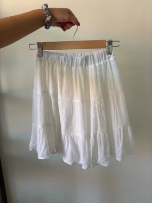 Vit volangkjol från Stradivarius - Säljer en superfin vit kjol från Stradivarius med volangdetaljer och resår i midjan. Kjolen är kort och har en luftig, flowy känsla som passar perfekt till varma dagar. 