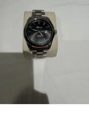 Klassisk silverfärgad herrklocka - Stilren klocka med rund svart urtavla och datumvisning. Armbandet är i metall med silverfärg och har en klassisk länkdesign. Urtavlan har tydliga markeringar och quartz-urverk. Perfekt accessoar för dig som gillar en tidlös look.