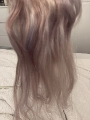Vågiga löshår clips i askblond - Säljer ett set vågiga löshår clips i en snygg askblond nyans. Håret är långt och har en naturlig glans med mjuka lockar. Clipsen är fästa på en tunn remsa för enkel applicering och styling. Perfekt för dig som vill ha extra volym och längd.