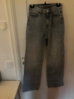 Ljusblå raka jeans med hög midja - Säljer ett par ljusblå jeans med raka ben och hög midja. Jeansen har klassiska fem fickor och en avslappnad passform. Materialet är denim i bomull och de har en snygg tvättad look som ger en vintagekänsla.