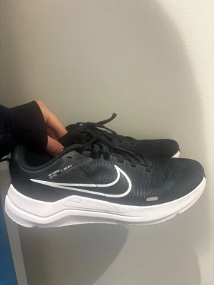 Svarta Nike sneakers med vit sula - Snygga svarta sneakers från Nike med klassisk vit sula och vit swoosh-logga på sidan. Skorna har snörning och en sportig, modern design som passar perfekt till streetwear och vardagsoutfits. Tillverkade i textilmaterial för en lätt och bekväm känsla. Som nya! Inga defekter! 