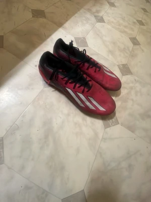 Adidas speedportal fotbollskor - Säljer ett par snygga fotbollsskor i rött med vita detaljer och svarta skosnören. Skorna har en modern, strömlinjeformad design och dobbar för bra grepp på planen. Ovandelen är i syntetmaterial och sulan är gjord för spel på gräs. Skorna är elite högsta model. Kan mötas i Stockholm om de  krävs 