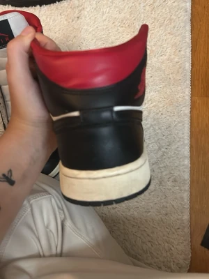 Svarta och röda höga sneakers - Snygga höga sneakers i svart och rött med vit sula. Skorna har en klassisk siluett och är tillverkade i läder med textilfoder. Perfekta för dig som vill ha en stilren och sportig look.