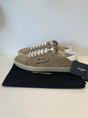 Beige Saint Laurent sneakers i mocka - Snygga beige sneakers från Saint Laurent i mjuk mocka med vit sula och vita skosnören. Skon har handskriven logga på sidan och vit detalj vid hälen. Perfekta för en clean och stilren look.