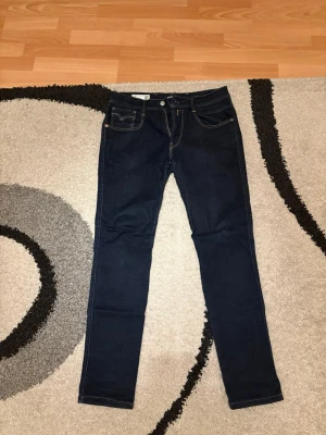Mörkblå skinny jeans från Replay - Snygga mörkblå skinny jeans från Replay med klassisk femficksdesign och kontrastsömmar. Jeansen har normal midja och smal passform hela vägen ner. Perfekta för dig som gillar en stilren och enkel look. Loggan där bak är lite sönder så kan gå ner yttligare ifall önskad.
