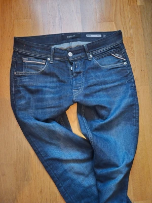 Mörkblå jeans från Replay - Snygga mörkblå jeans från Replay med klassisk femficksmodell och kontrastsömmar. Jeansen har en rak passform och detaljer som läderpatch med logga bak samt Replay-märke på fickan. Tillverkade i slitstarkt denimtyg.