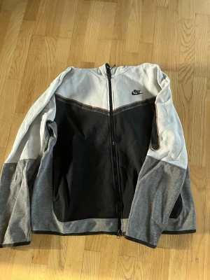Nike tech  - Nike ziptröja med färgblock i svart, ljusgrått och mörkgrått. Tröjan har hel dragkedja framtill, lång ärm och liten Nike-logga på bröstet. Perfekt för en sportig och avslappnad stil. Det är en Nike tech. Ganska använd men absolut inget som synns. 