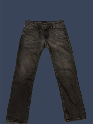 Gråa jeans från Jack&Jones - Snygga gråa jeans med raka ben och diskreta slitningar. Klassisk femficksmodell med knappgylf och bälteshällor. Jeansen har en tvättad look som ger en avslappnad vibe och passar perfekt till en streetwear-stil.