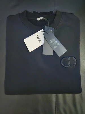 Svart stickad tröja från Dior - Snygg svart stickad tröja från Dior med rund halsringning och diskret CD-logga broderad på bröstet. Tröjan har ribbade muddar vid hals, ärmslut och nederkant. Perfekt för dig som gillar stilrena och exklusiva plagg.