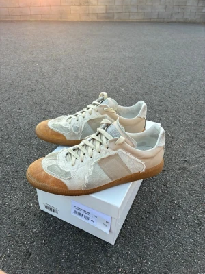 Äkta sällsynta maison margiela skor - Sällsynt par av maison margiela i nyskick med en sjukt fet design. Snygga sneakers i beige och vitt med slitna detaljer och klassisk gummisula. Skorna har lågt skaft, vita snören och paneler i mocka och tyg. Perfekta för dig som gillar en avslappnad och trendig stil.