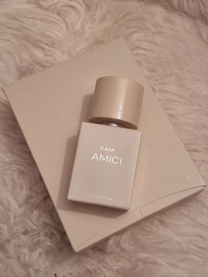 CAIA AMICI Eau de Parfum - Snygg parfymflaska från CAIA, doften AMICI. Flaskan är fyrkantig och har en stilren, ljusbeige design med ett matchande lock. Perfekt för dig som gillar minimalistisk och modern stil. Kommer i originalförpackning.