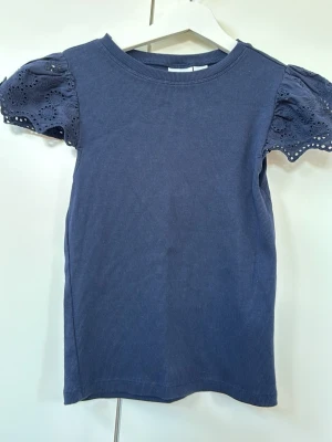 Mörkblå topp med spetsärmar Gina Tricot - Supersnygg mörkblå topp från Gina Tricot med ribbad struktur och korta puffärmar i spets med broderade detaljer. Perfekt för dig som vill ha en enkel men ändå unik topp till garderoben.