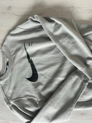 Grå sweatshirt från Nike - Snygg grå sweatshirt från Nike med svart logga och trycket '20/21' på bröstet. Tröjan har rund halsringning, ribbade muddar och är tillverkad i mjukt bomullsmaterial. Perfekt för en avslappnad och sportig stil.