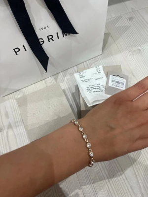 PILGRIM •Guldigt armband med glittrande stenar - Snyggt armband från Pilgrim i guldfärgad metall med runda, glittrande stenar som ger en lyxig känsla. Perfekt accessoar för att lyfta din outfit med lite extra bling. Lätt att matcha med andra smycken och passar till många stilar. Säljer eftersom att jag har smal handled så den passar mig inte perfekt 