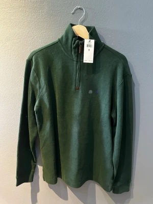 Grön half-zip tröja Polo Ralph Lauren - Mörkgrön långärmad tröja från Polo Ralph Lauren med half-zip och hög krage. Tröjan har diskret logga på bröstet och är tillverkad i mjukt material. Perfekt för lager-på-lager och en clean look.