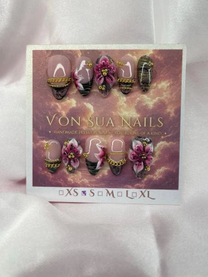 Zarina (S);Medium Almond - Unika handgjorda press-on naglar i en medium lång mandelform med nude bas, dekorerade med 3D-blommor i rosa och gulddetaljer, små kedjor och svarta spetsmönster. Handgjorda och perfekta för dig som vill ha något extra. S: 15 mm, 11,5 mm, 12 mm, 11 mm, 9 mm 