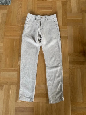 Beige linnebyxor från NN07 - Snygga beige linnebyxor från NN07 med raka ben och klassisk passform. Byxorna har bälteshällor, knappgylf och sidofickor. Tillverkade i ett luftigt linnetyg som passar perfekt för varma dagar.