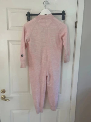 Ljusrosareima ull body underställ - Mysig ljusrosa body med långa ärmar och ben, tillverkad i 80% ull och 20% polyester. Perfekt för lager-på-lager och håller dig varm. Enkel och stilren design utan synliga detaljer framtill. Fick skick med något missfärgad och nopprig i muddarna