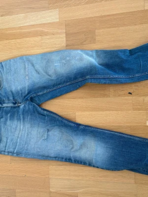 Calvin Klein jeans med unika lagningar  - Ett par blå jeans med tydliga slitningar och tvättade detaljer på låren och knäna. Jeansen har en klassisk rak passform och är gjorda i denim. Perfekta för en avslappnad och trendig look. Har unika och coola lagningar. W31 L 32