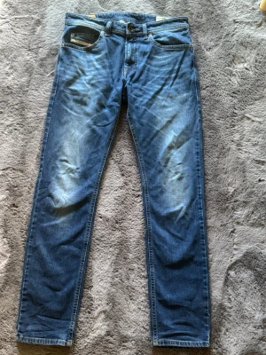 Diesel Thommer jeans 32-32 - Säljer ett par blå jeans med raka ben och snygga slitningar på framsidan. Jeansen har klassisk femficksdesign och kontrastsömmar. Materialet är denim i bomull och passformen är normal. Perfekta för en avslappnad och trendig stil.