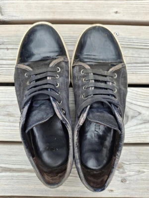 Lanvins sneakers med gummisula - Lanvin sneakers i svart läder, originalpåse ingår. Köpta begagnade och använda varsamt i cirka ett år. Skosnöre och sula är skadat. Kom med frågor angående skadorna. Nypris cirka 5 000 kr. Påse till skorna ingår. Prisförslag fungerar vid snabb affär.