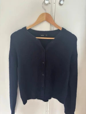 Mörkblå kofta - Mysig mörkblå kofta från LMTD med rund halsringning och knäppning framtill. Tillverkad i ett mjukt, fluffigt material som ger en avslappnad look. Perfekt att slänga över en t-shirt eller topp för extra värme.