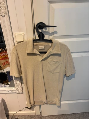 Beige frottéskjorta från Gant - Snygg beige skjorta från Gant i mjuk frotté med klassisk krage och bröstficka. Kortärmad modell som passar perfekt till varmare dagar och ger en avslappnad men stilren look.
