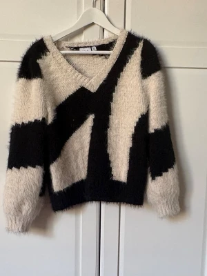 Beige och svart stickad tröja VILA - Säljer en fluffig stickad tröja från VILA i beige och svart med coolt grafiskt mönster. Tröjan har V-ringning, långa ärmar och är gjord i ett mjukt, lurvigt material som känns riktigt mysigt. Perfekt för dig som gillar statement-plagg!
