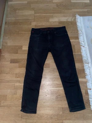 Svarta slim fit jeans från Hugo - Snygga svarta slim fit jeans från Hugo med klassisk femficksdesign och diskret röd logga i linningen. Jeansen har en modern passform och är tillverkade i ett stretchigt denimtyg som ger både stil och komfort.//PRIS KAN DISKUTERAS!!