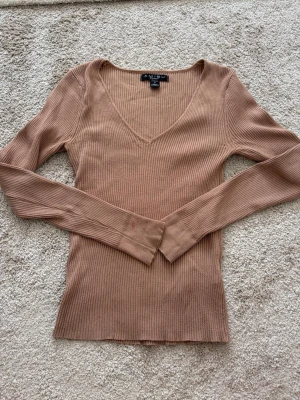 Beige ribbstickad tröja med v-ringning - Snygg beige ribbstickad tröja från Arole U med djup v-ringning och långa ärmar. Tröjan har en figurnära passform och breda muddar vid ärmsluten. Perfekt att styla med jeans eller kjol för en trendig look.