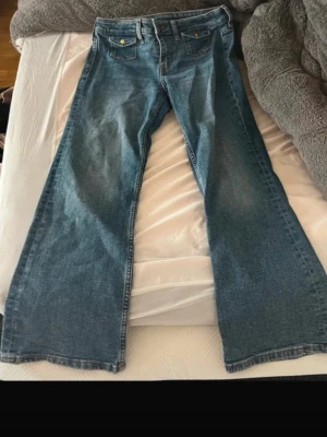 Blå bootcut jeans med fickor - Nya med prislapp, Säljer ett par klassiska blå bootcut jeans med två framfickor och två bakfickor. Jeansen har normal midja och är tillverkade i ett slitstarkt denimtyg. Perfekta för en avslappnad och trendig look.