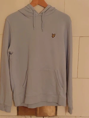 Ljusblå hoodie från Lyle & Scott - Säljer en stilren ljusblå hoodie från Lyle & Scott med klassisk gul logga på bröstet. Hoodien har huva med dragsko och en stor magficka framtill. I absolut nyskick, kommer från ett djur och rökfritt hem. Tröjan är ljusblå men svårt att fånga på bild.