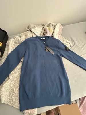 Stone island tröja - Snygg blå stickad tröja från Stone Island med rund halsringning och lång ärm. Tröjan har en klassisk patch på vänster ärm och är tillverkad i mjukt stickat material. Perfekt för dig som gillar stilrena och trendiga plagg. Behöver sälja den för jag behöver pengar helt ny inte använd prislapp på. Den är M funkar S också