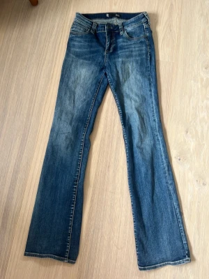 Blå bootcut jeans  - Snygga blå bootcut jeans med lätt slitna detaljer framtill och bakfickor. Klassisk femficksmodell med normal midja och dragkedja. Jeansen heter Natalie Botcut och köptes för 300 kr. 