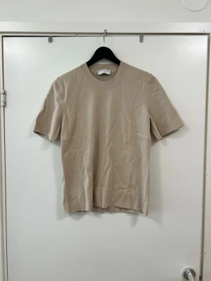 Beige t-shirt från Tiger of Sweden - Snygg beige t-shirt från Tiger of Sweden i mjuk bomull. Klassisk rund halsringning och korta ärmar. Enkel och stilren design som passar till det mesta. Perfekt basplagg för garderoben.