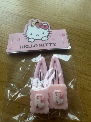 Hello Kitty rosa hårspännen - Söta hårspännen i ljusrosa plast med Hello Kitty-motiv. Spännena har en dekorativ kant och en liten 3D-bild av Hello Kitty med rosa rosett. Perfekta för att piffa upp frisyren med en gullig detalj.