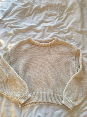 Beige stickad tröja med ballongärm - Mysig beige stickad tröja med rund halsringning och ballongärmar. Tröjan har ribbade muddar vid ärmslut och nederkant. Perfekt för lager på lager och enkel att matcha med olika stilar.